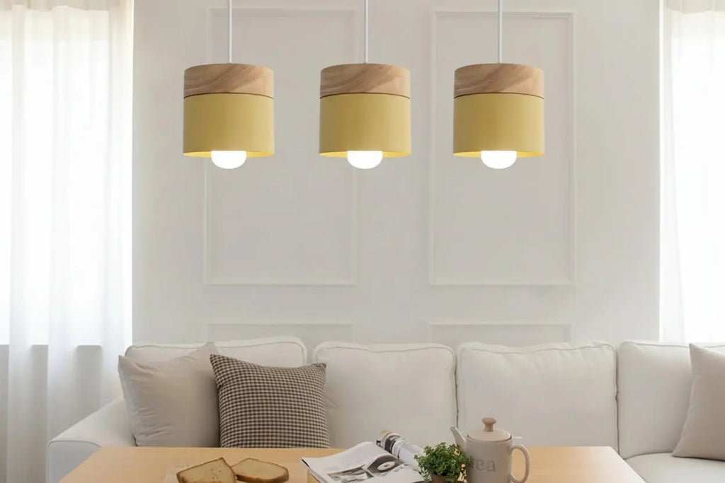 Three pendant lights with wooden tops and yellow shades hanging above a sofa.