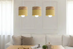 Three pendant lights with wooden tops and yellow shades hanging above a sofa.